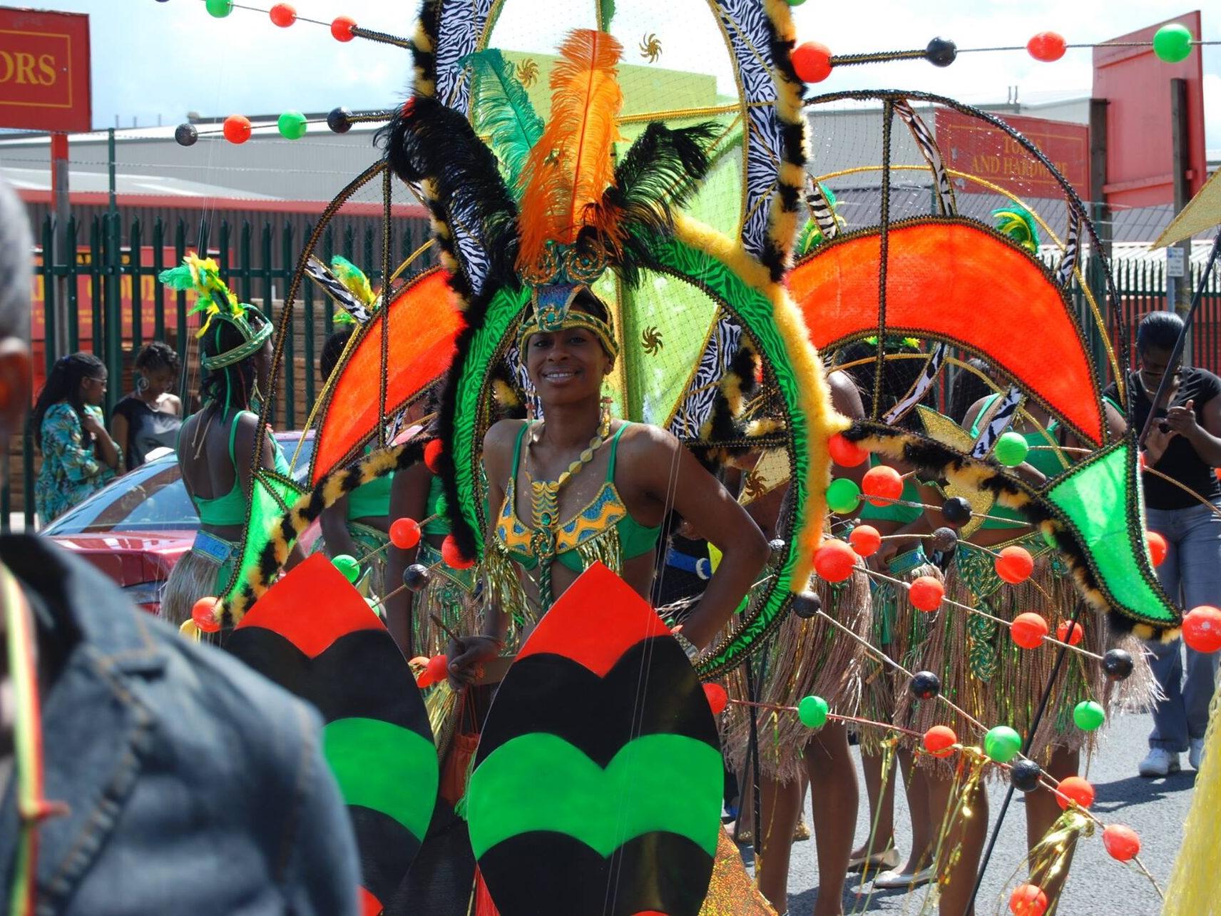 Elaborate mas band costume in green, orange and gold with feather headdress.