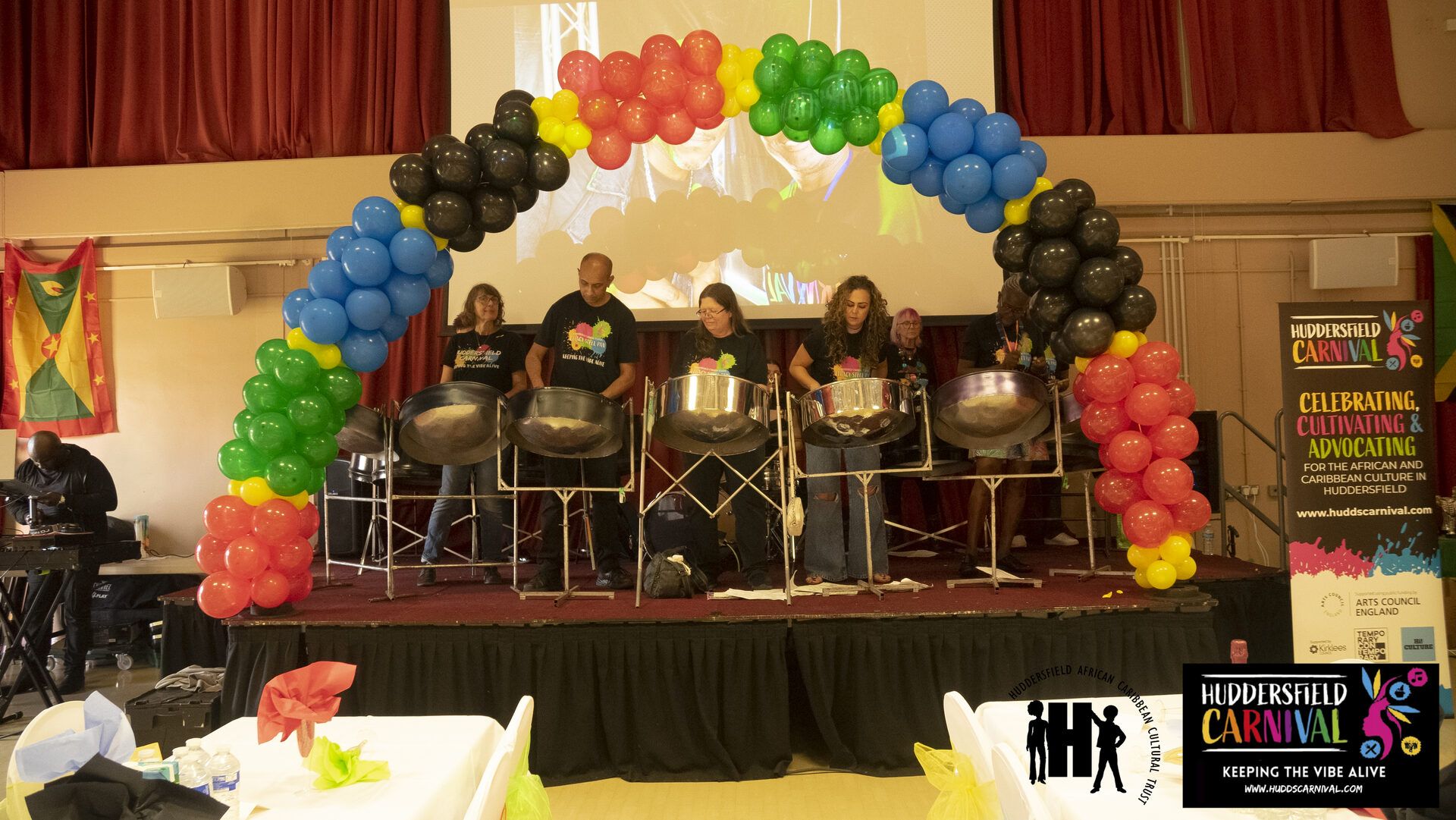 The Legacy Steel Band performing under a balloon arch in red, gold, green and black.