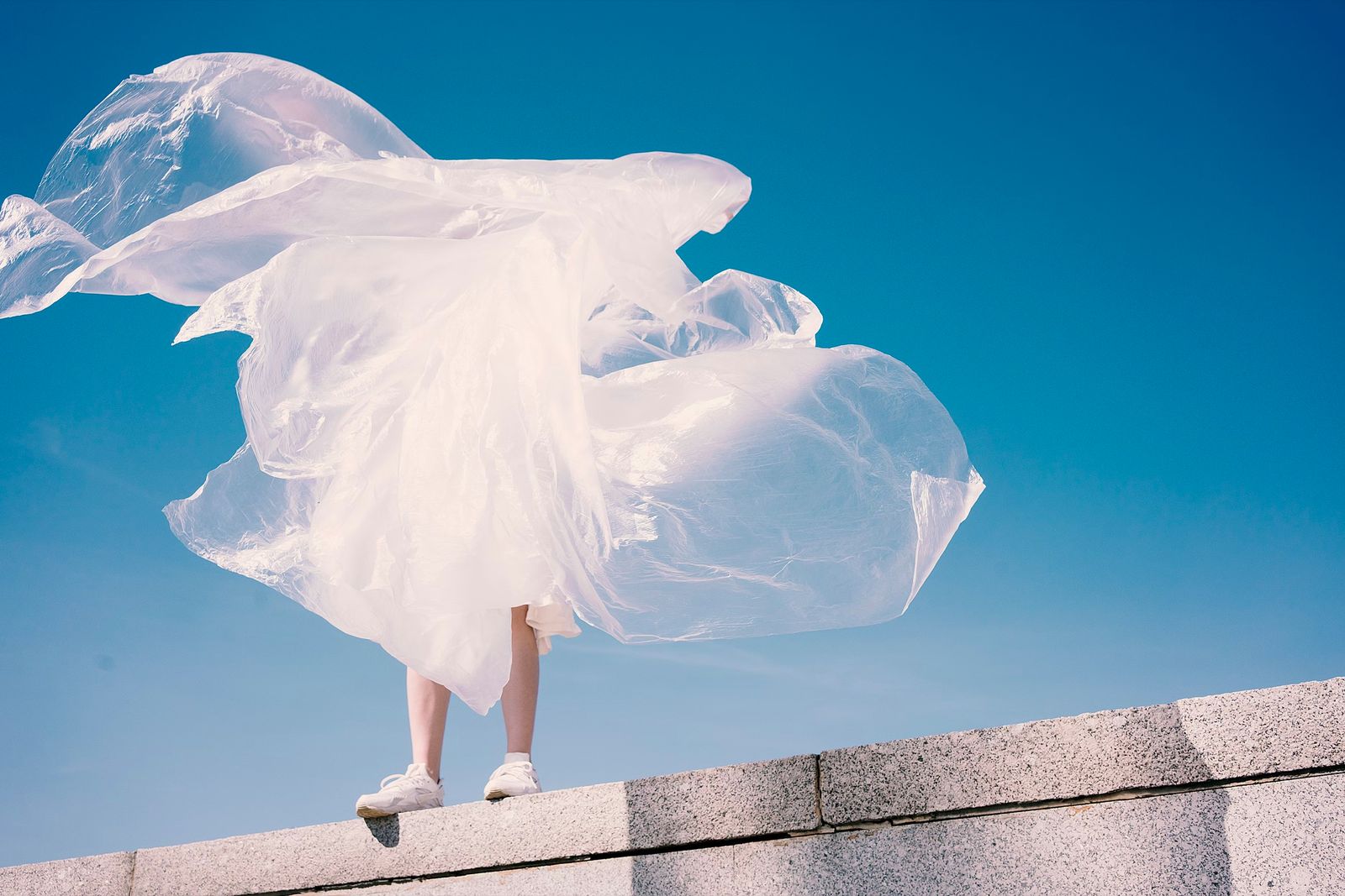 Person in a billowing white dress on a wall against a blue sky