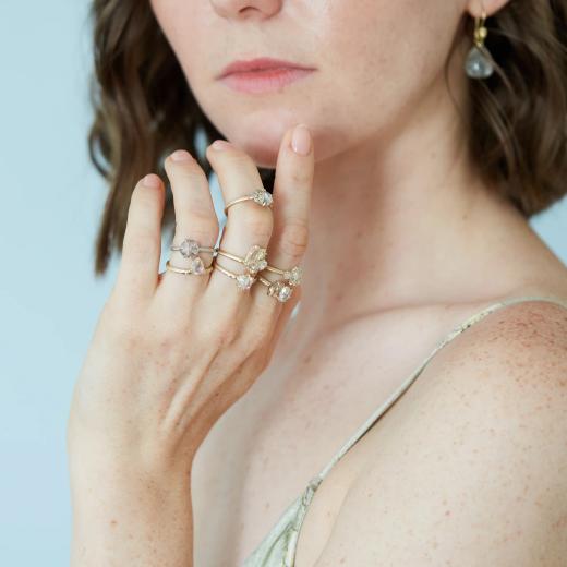 Hannah Blount model wearing a stack of handcrafted gemstone rings and a teardrop earring against a soft blue backdrop