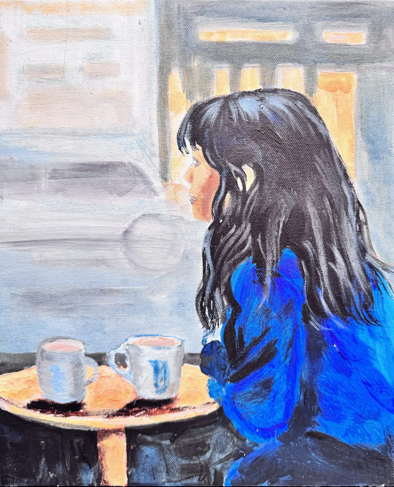 A woman with long dark hair in a blue jumper at a café table with two cups, looking out of a window