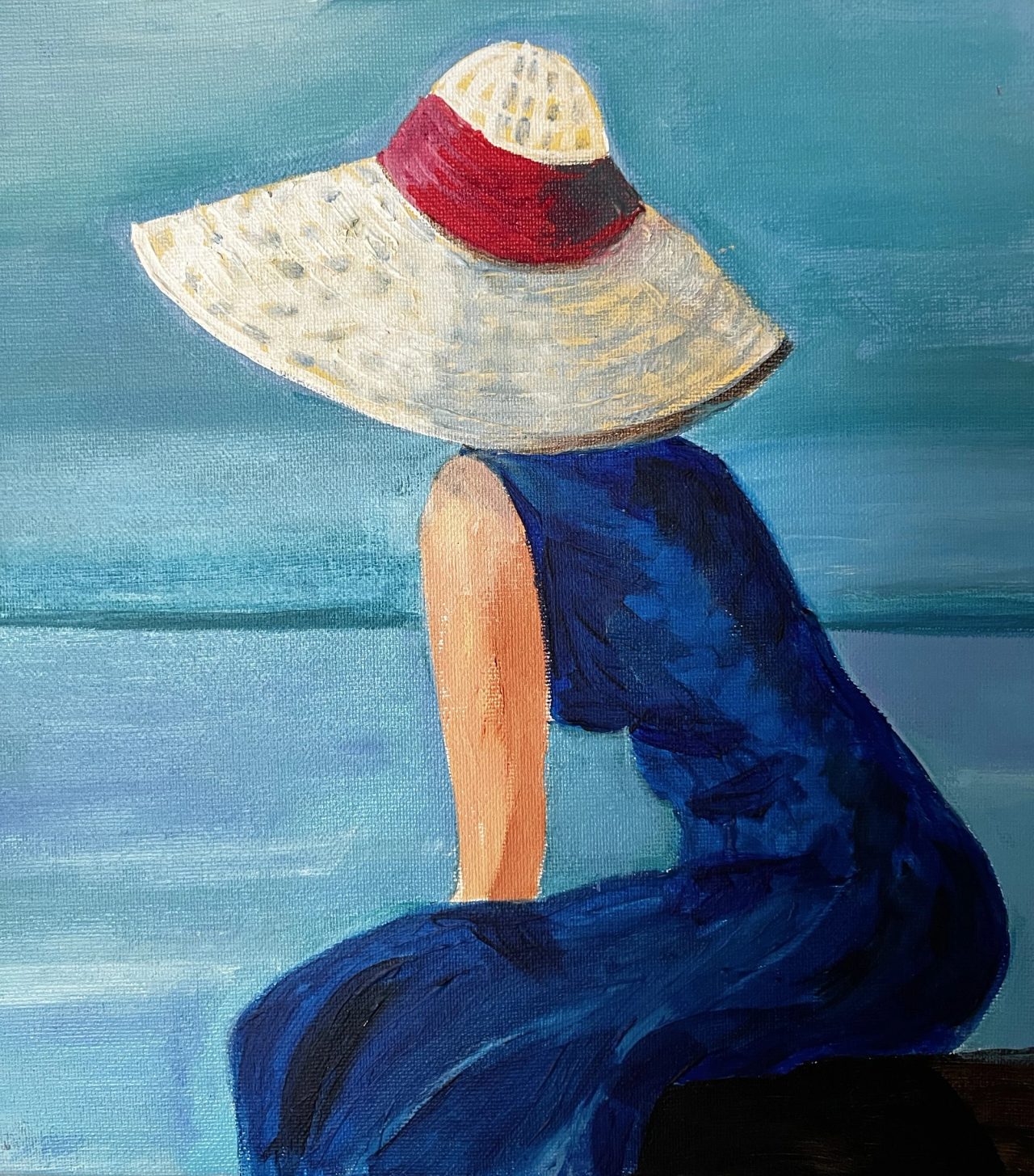 A woman in a wide straw hat with a red band and a blue dress, seen from behind, looking out to sea
