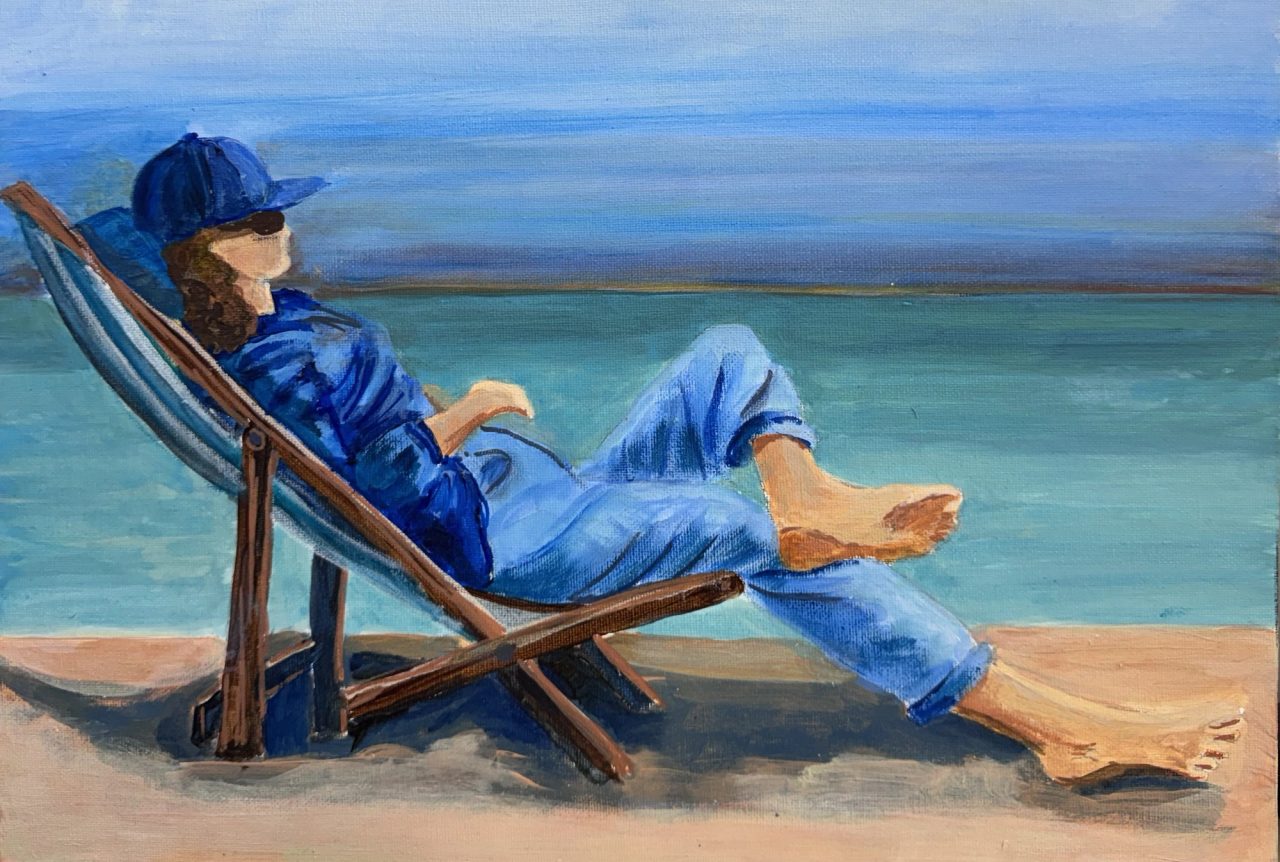A woman in a blue cap reclining barefoot in a deckchair by a turquoise sea