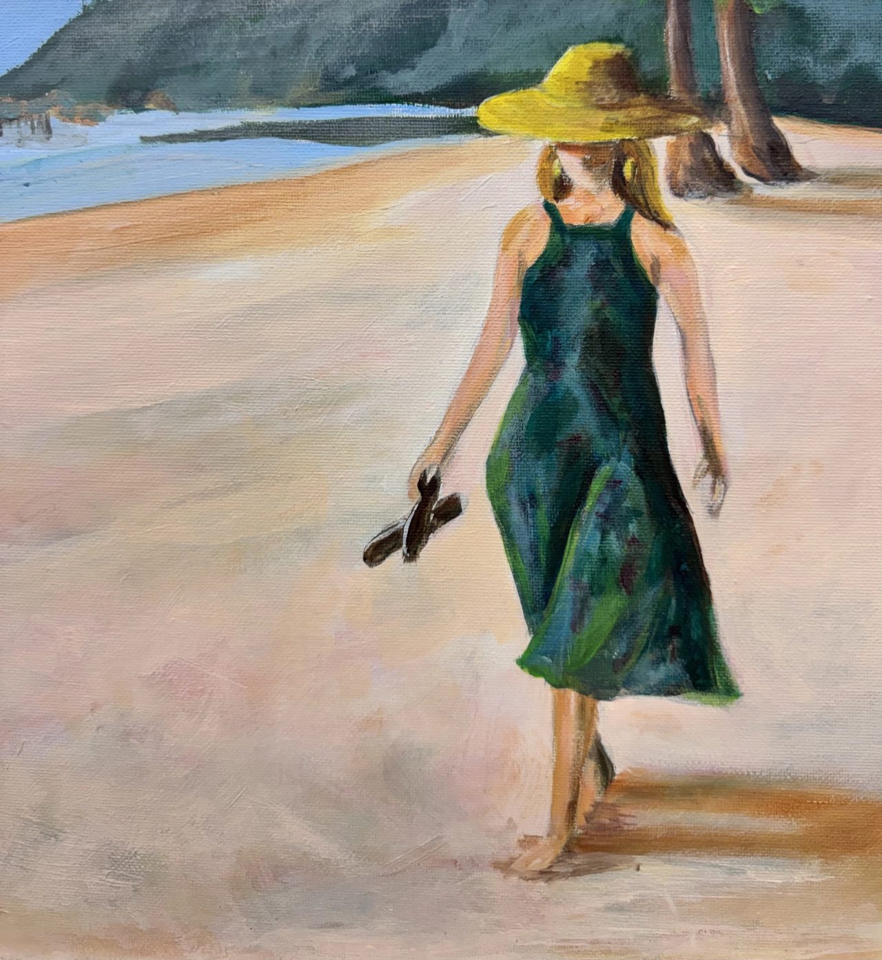 A woman in a yellow straw hat and green dress walking barefoot on a beach, carrying her sandals