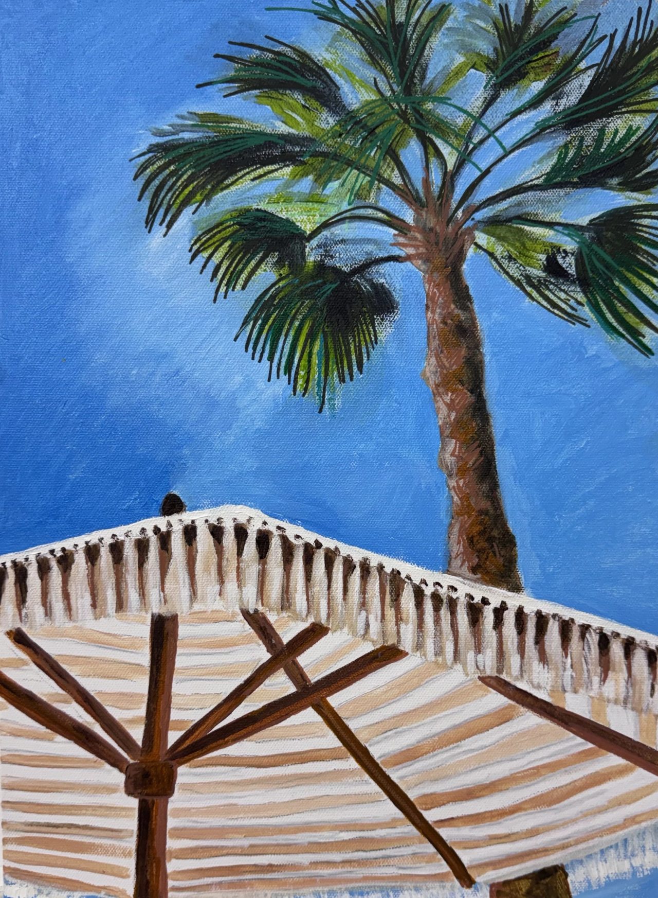 A palm tree against a blue sky above a striped fringed parasol
