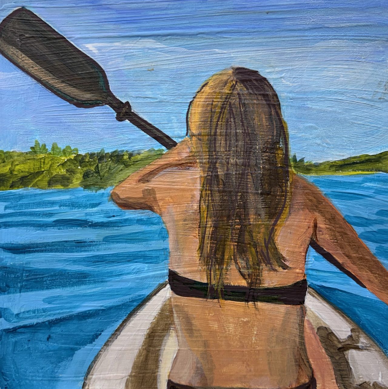 A woman with long hair paddling a kayak, seen from behind, towards a wooded shore