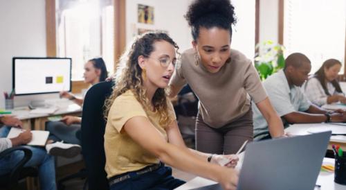 Two people looking at a laptop screen in an office environment