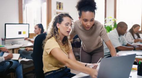 Two people looking at a laptop screen in an office environment