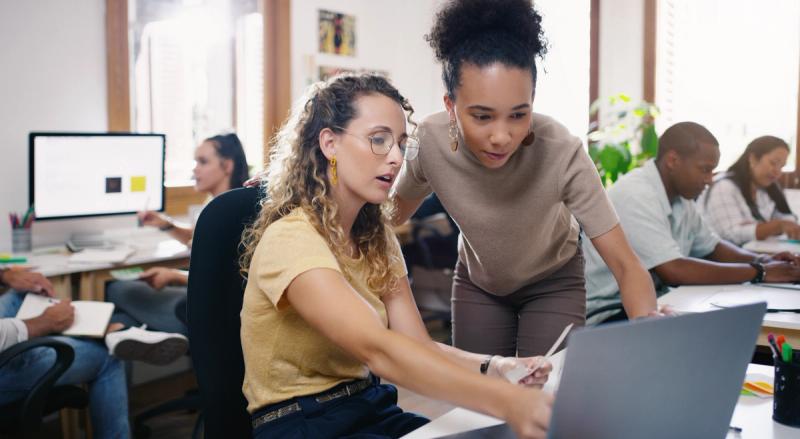 Two people looking at a laptop screen in an office environment