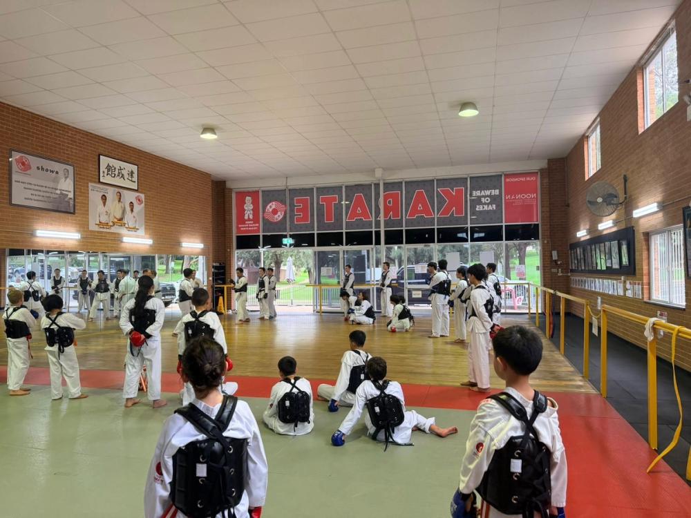 Karate class with kids and teens in protective gear listening before sparring in a dojo