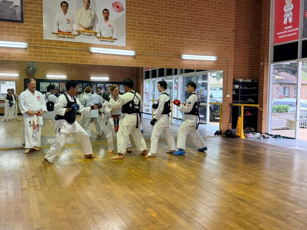 Karate students sparring in protective gear during dojo training on wooden floors