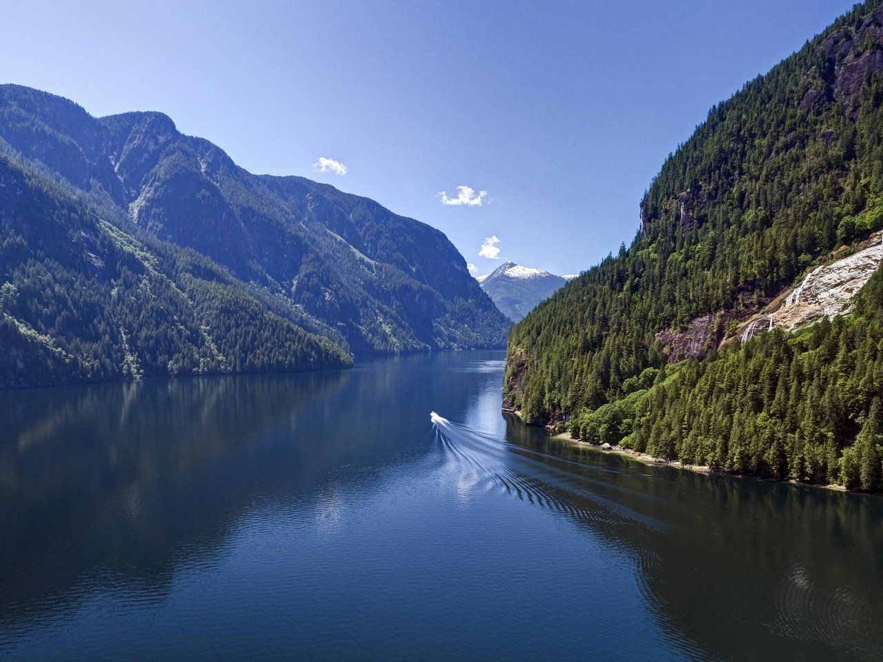 Aerial view of Princess Louisa Inlet with a boat travelling through calm water surrounded by forested mountains.