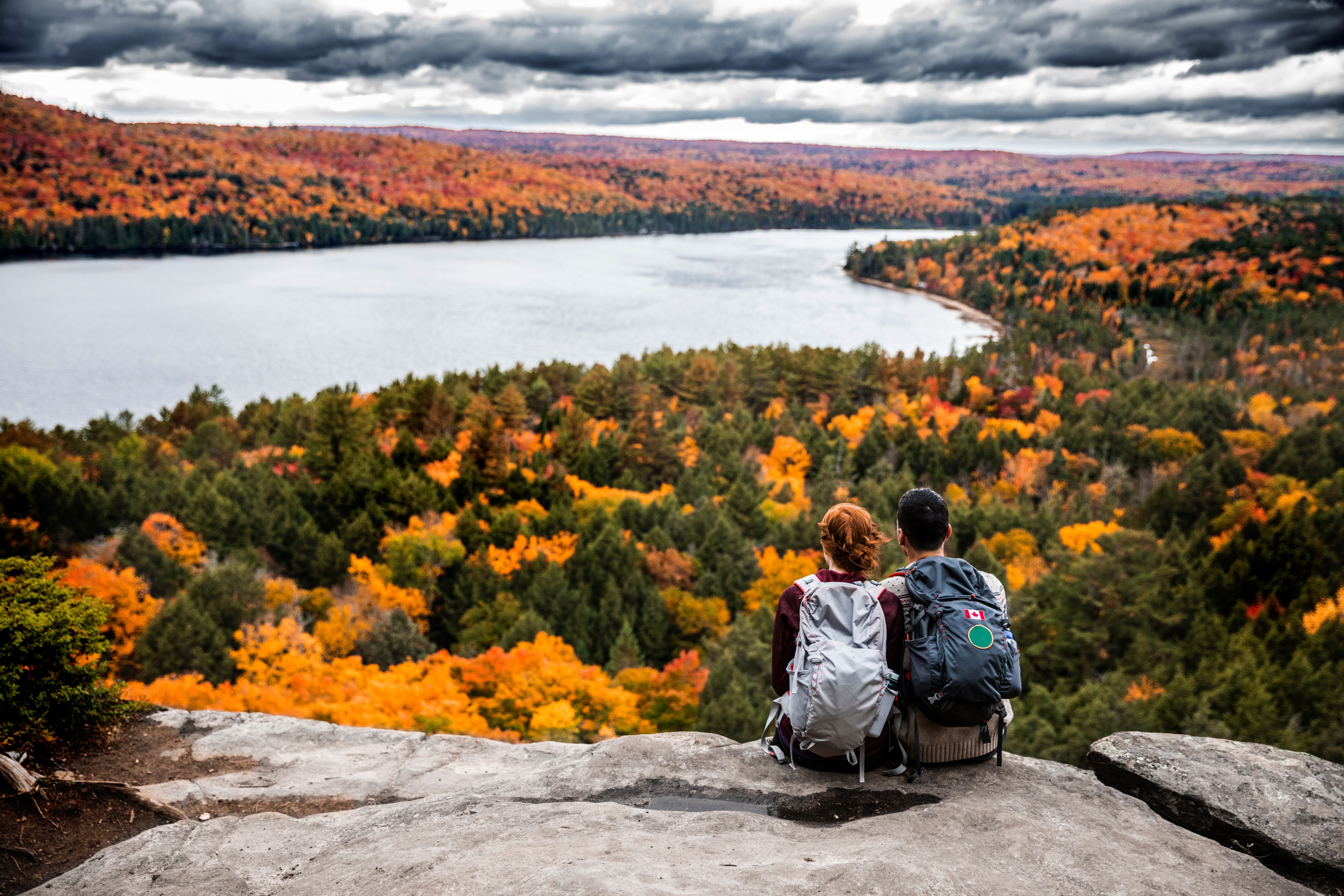 Two people sit on a rock looking over golden trees and a lake
