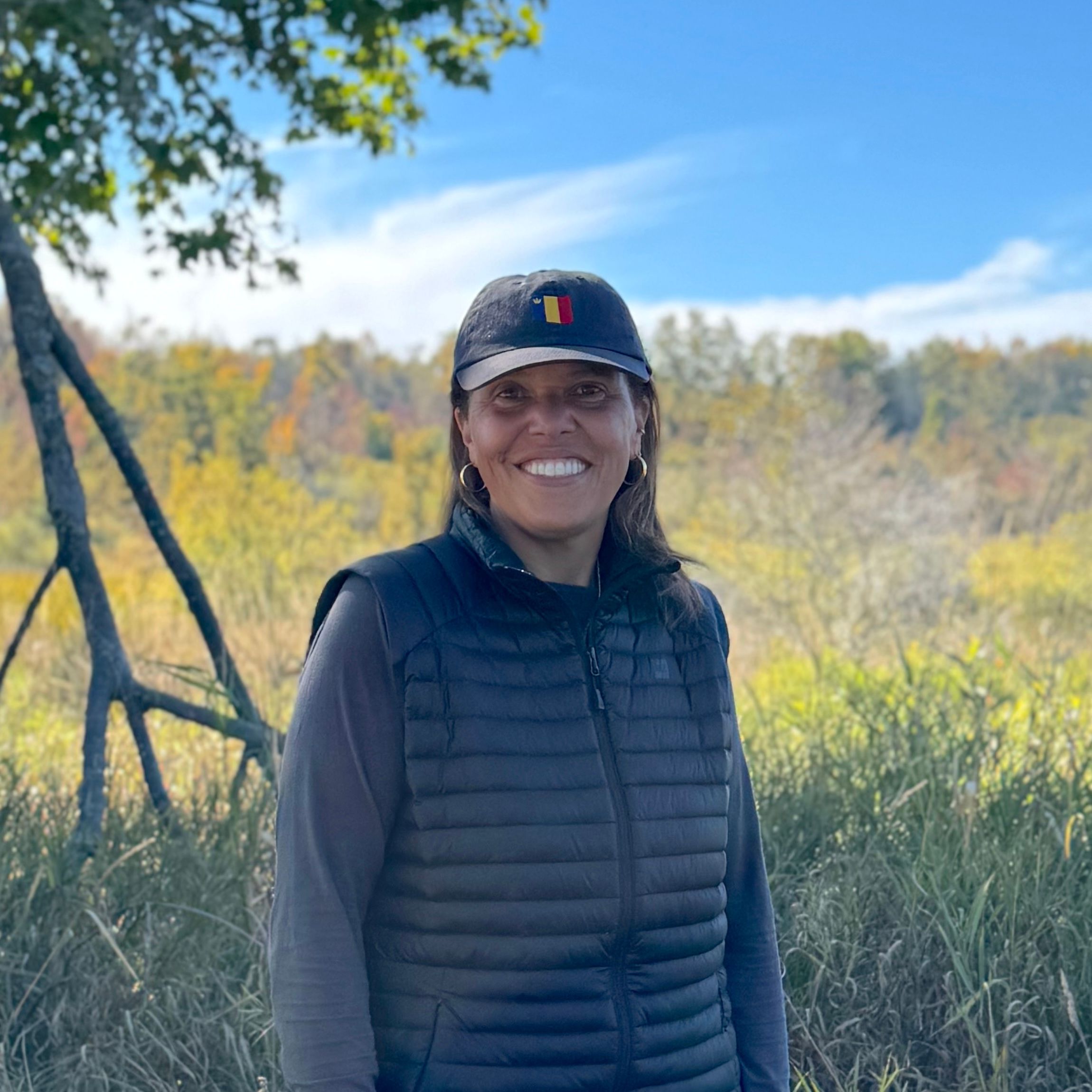 Gina smiling in a grassy meadow on a bright fall day.