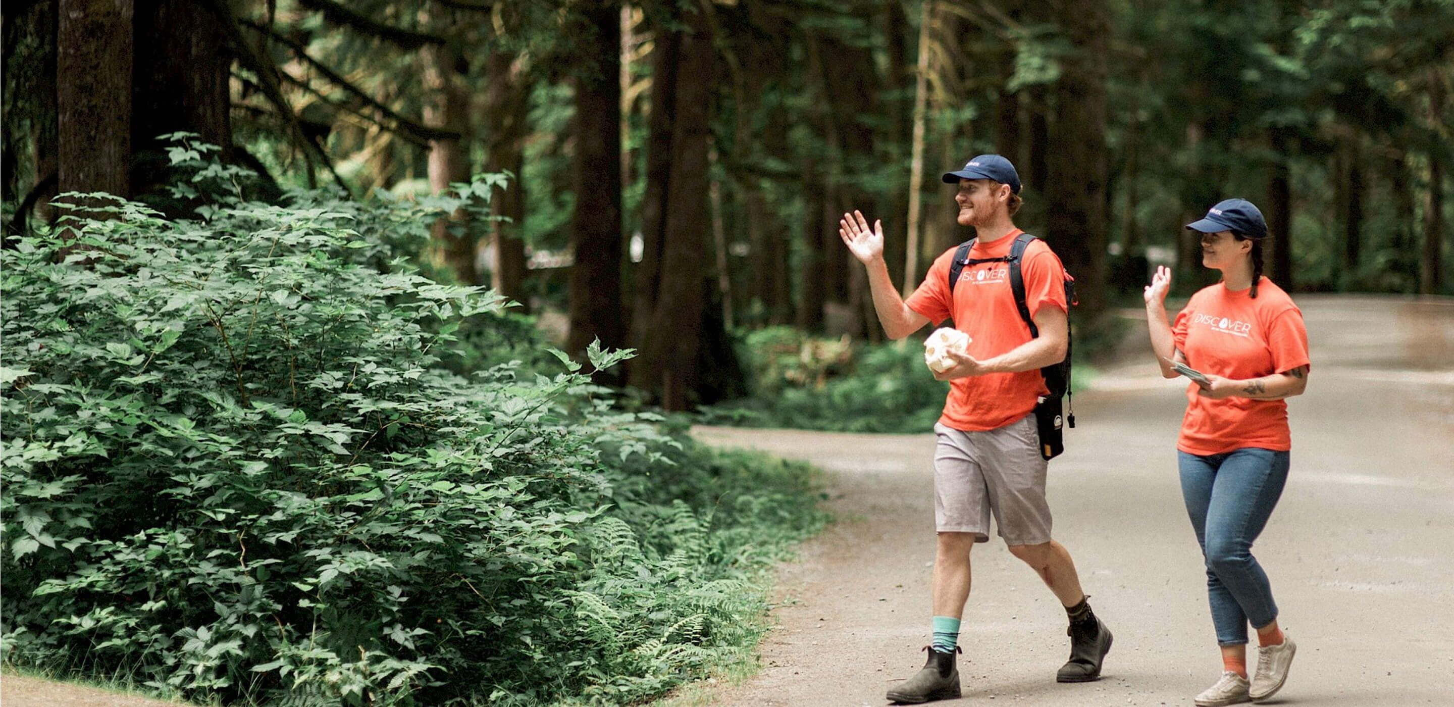 Two Discover Parks Ambassadors wave hello in a forest setting