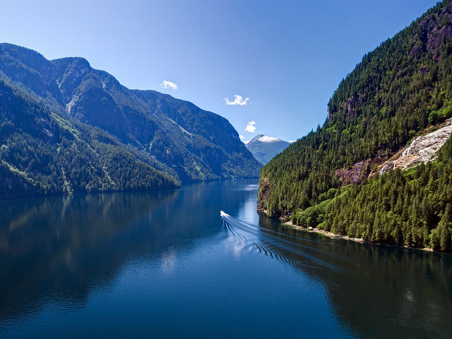 A large body of deep blue water between mountains covered in trees