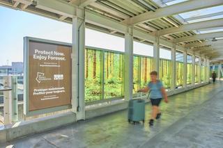 Tourist walks through Canada Line walkway with BC Parks Foundation wrap in background