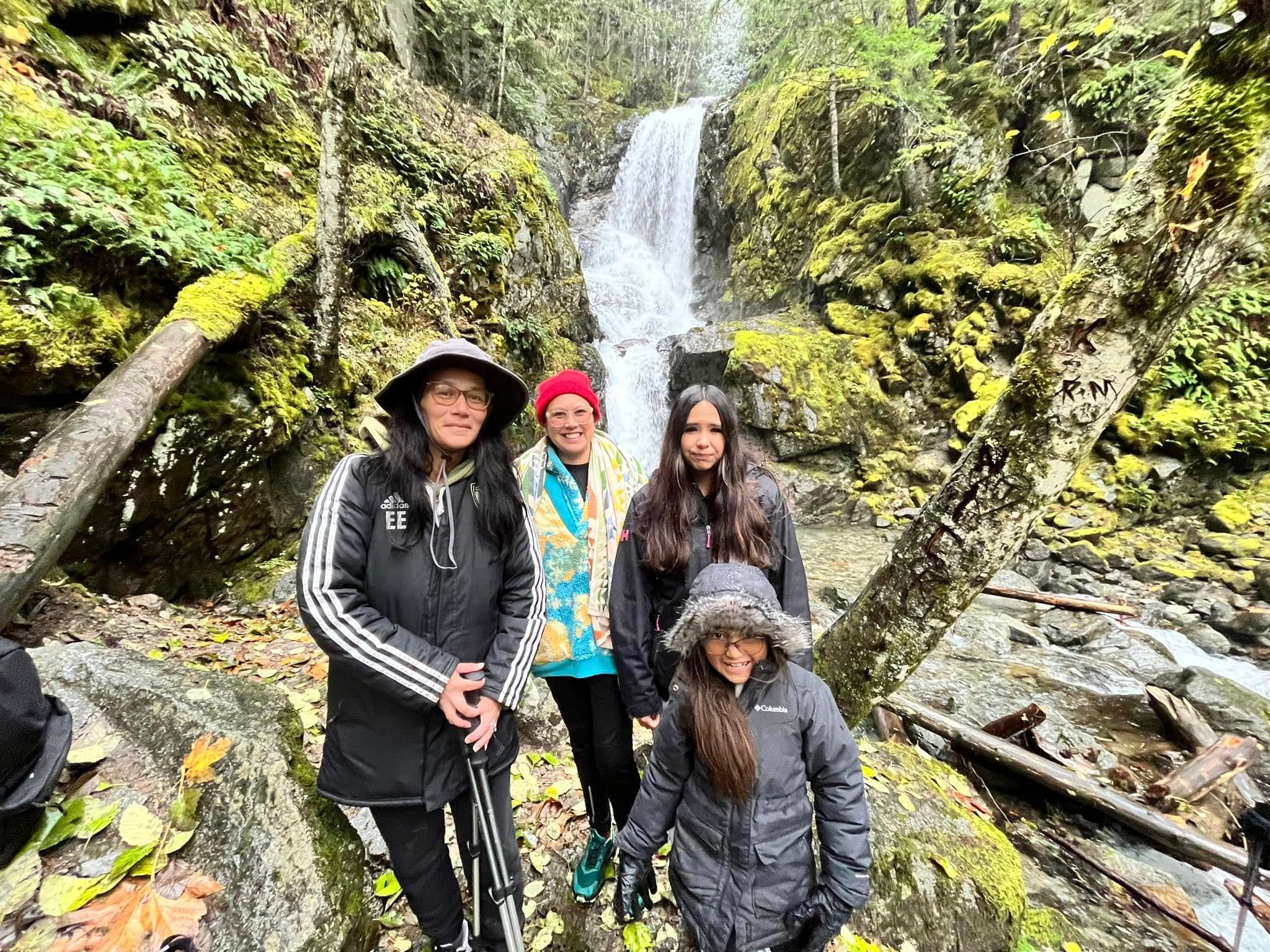 Four people pose for picture in front of waterfall.