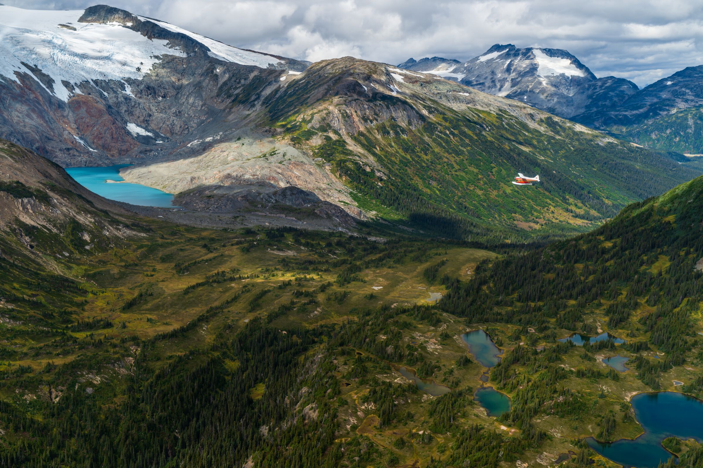 A wide view of grassy valleys, lakes and snowcapped mountains.