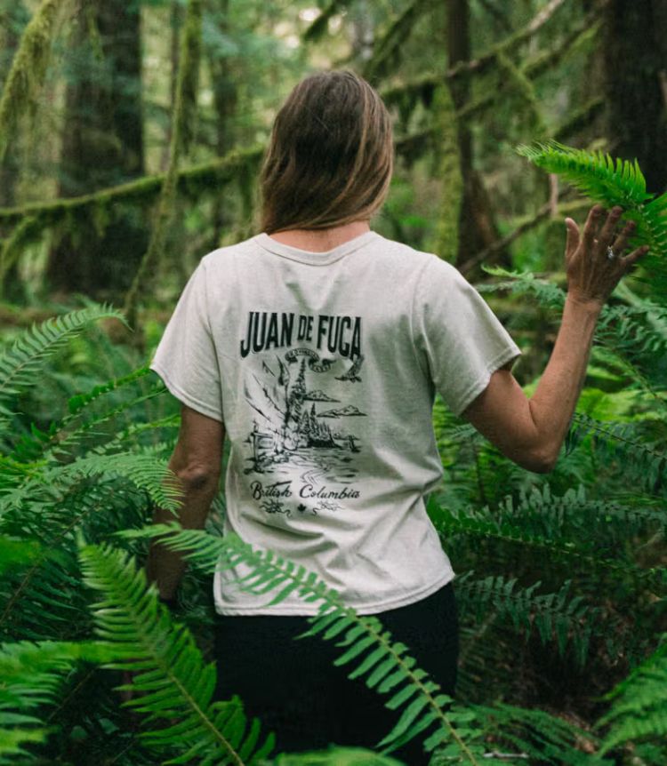 A person walks through a forest, wearing a BC Parks x Juan de Fuca shirt