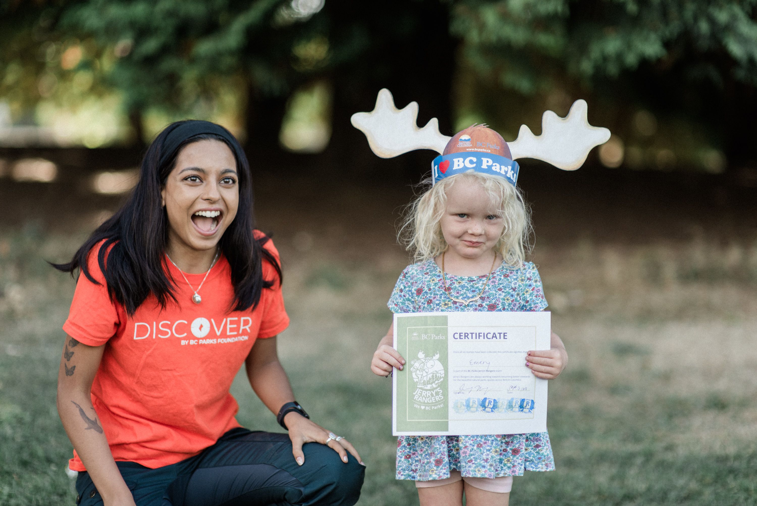 A Discover Parks Ambassadors smiles with a child holding their program certificate
