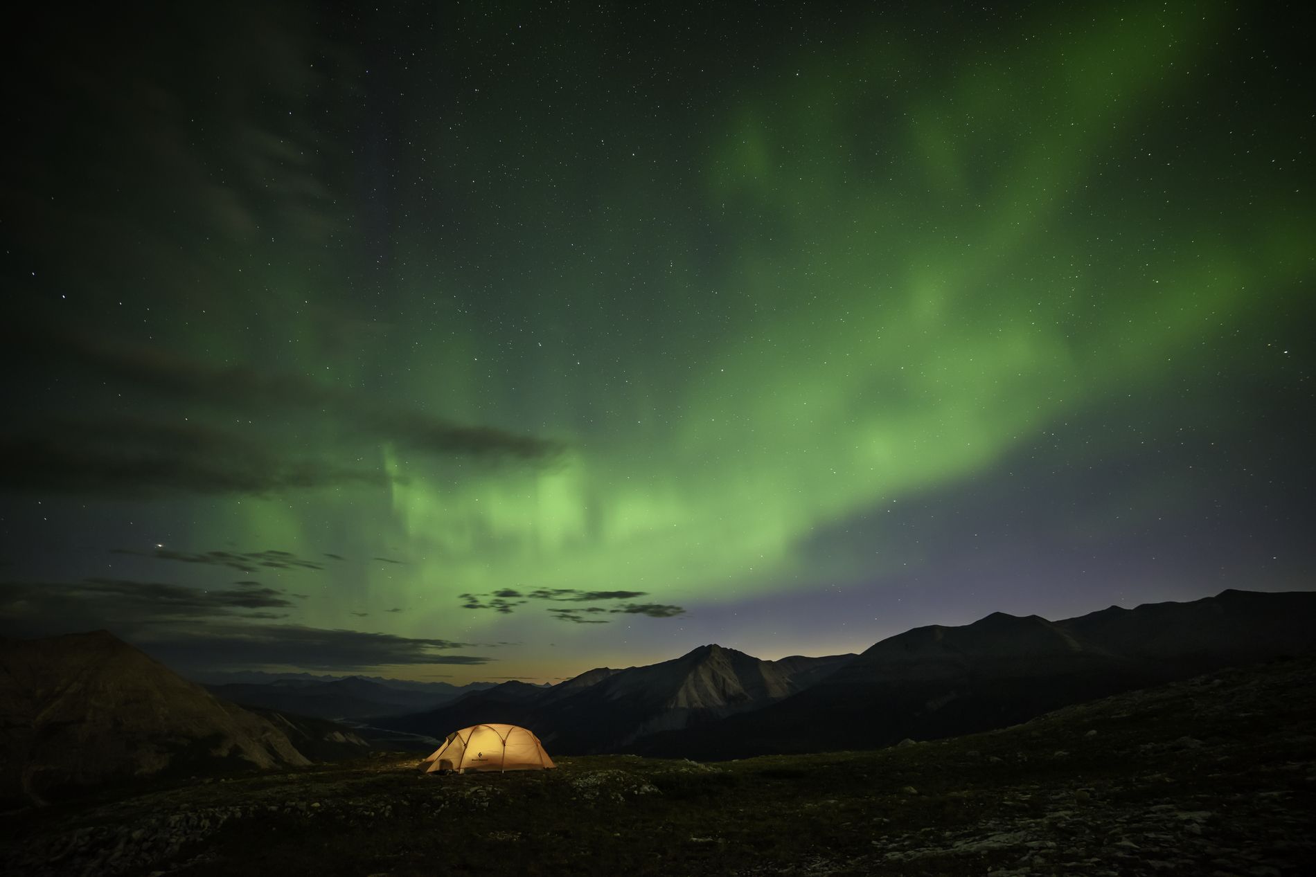 A tent is lit up with lights, underneath bright green northern lights