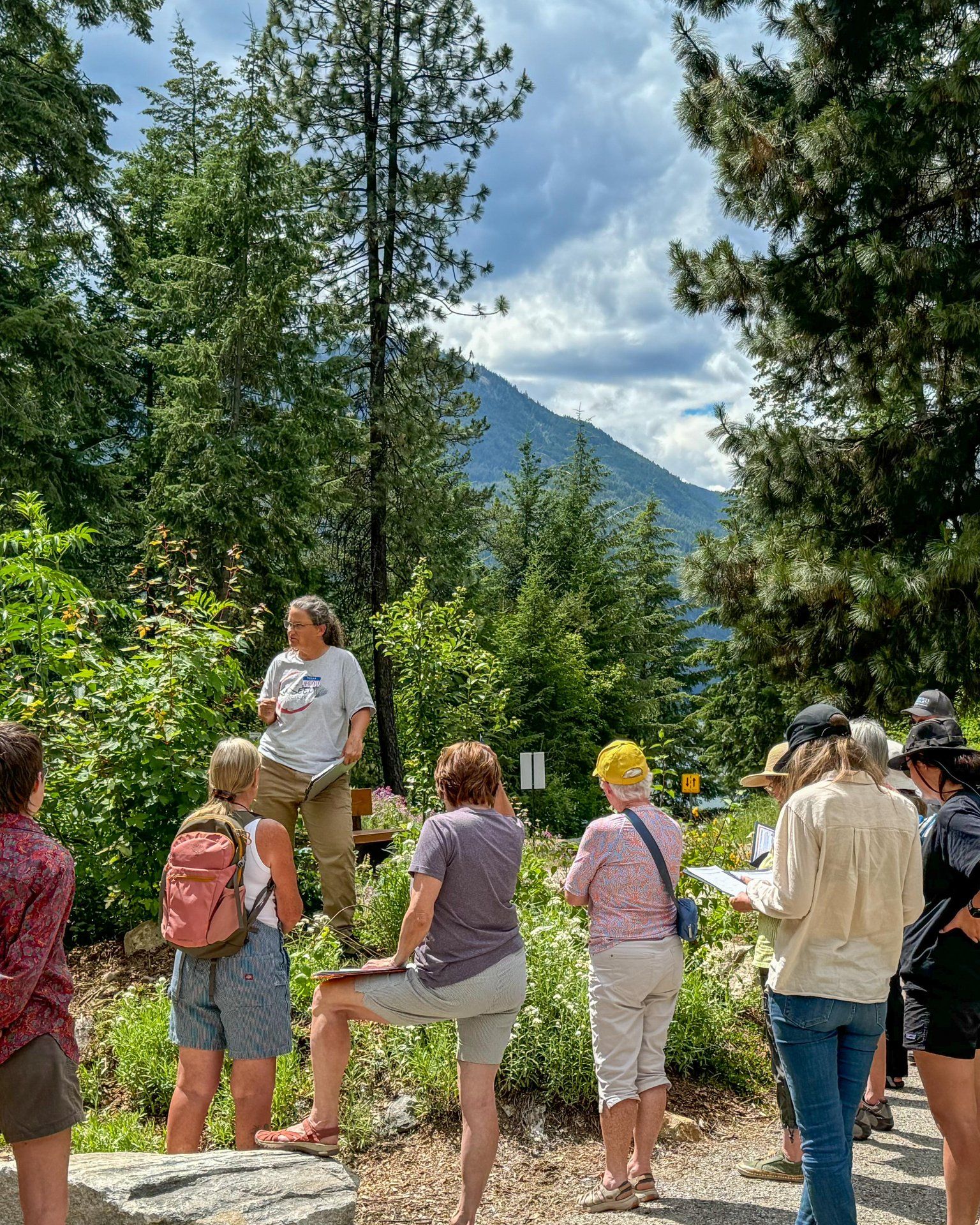 Park guide speaking to a group on a forest trail with mountains in the background.