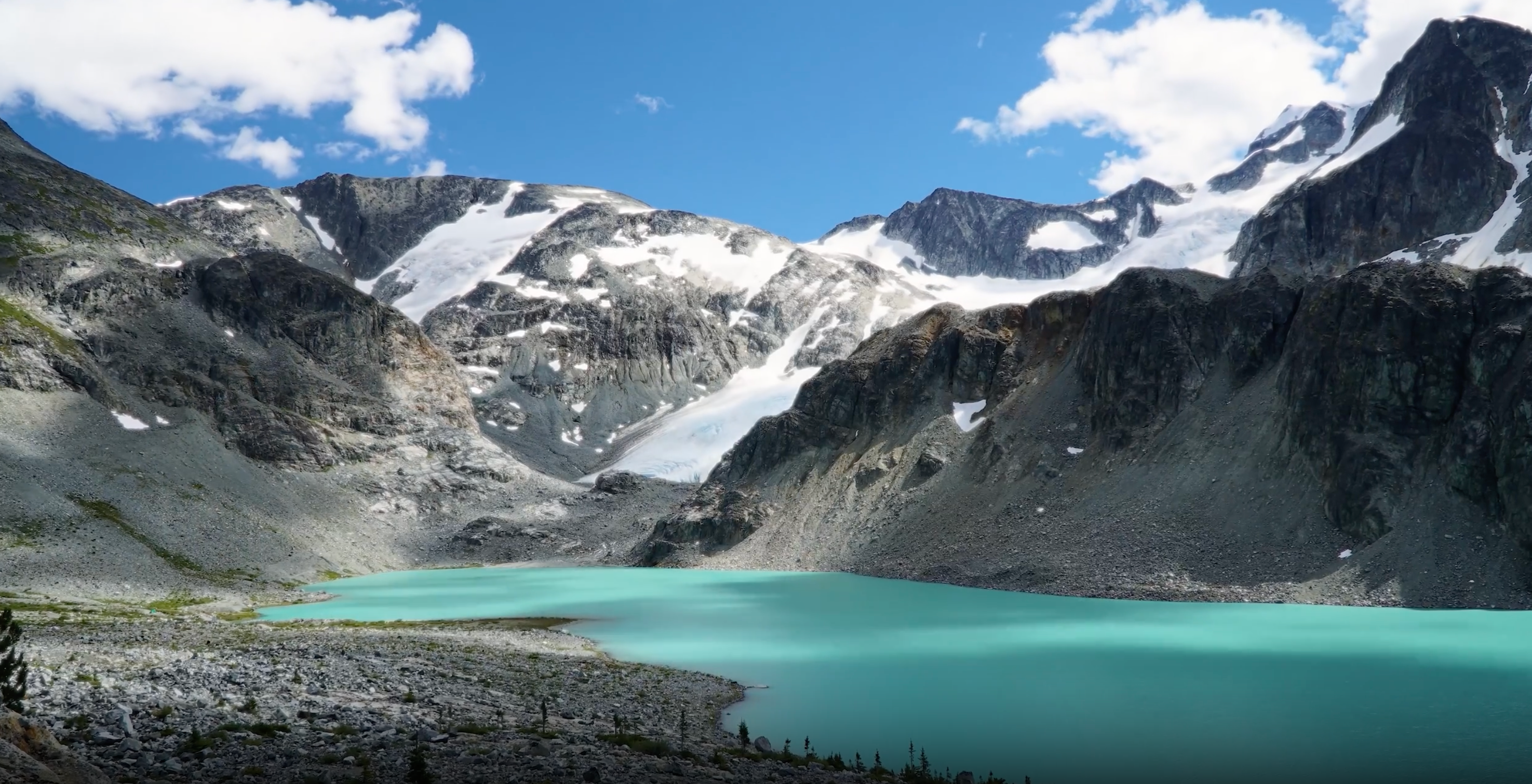 Turquoise alpine lake surrounded by rocky mountains with patches of snow