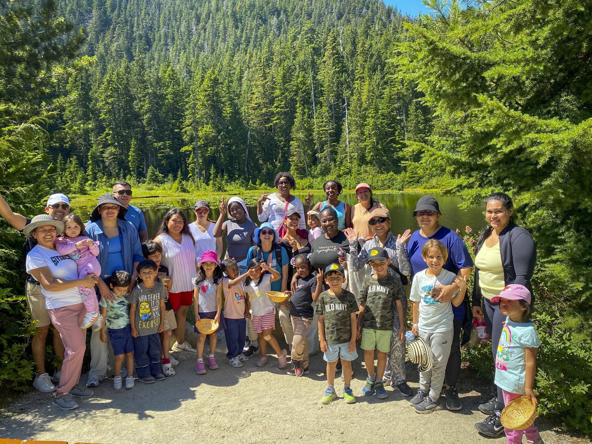 Group of families and children gathered by a small lake in a forest.