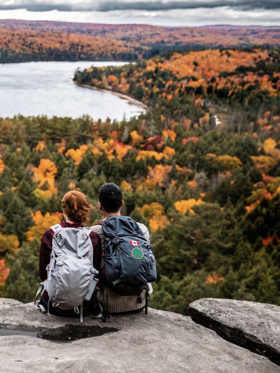Two people with backpacks sit together on top of a viewpoint