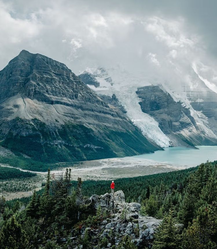A person stands on top of a rock and peers over 