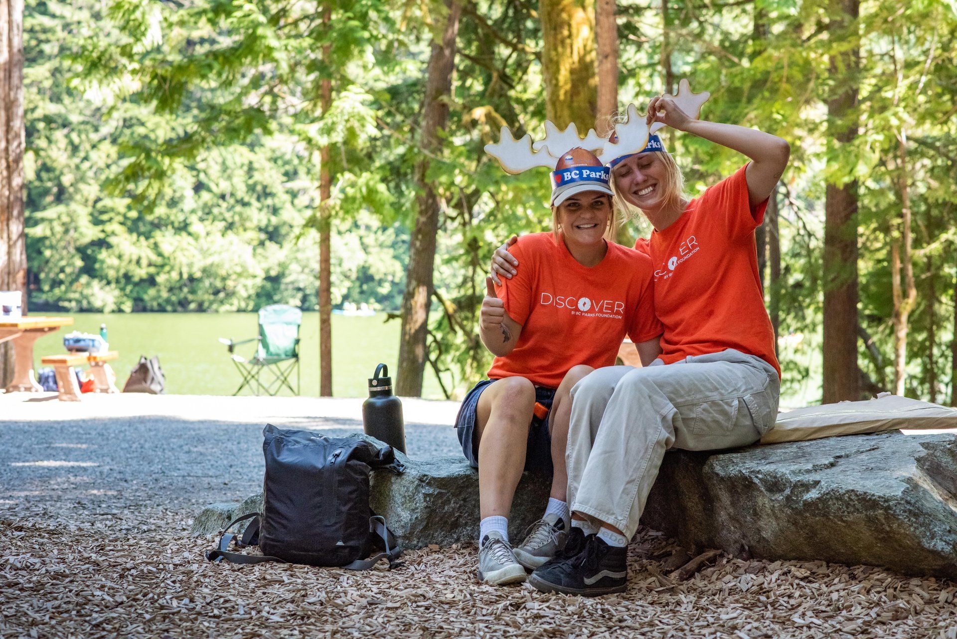Two park ambassadors sitting by a lakeside picnic area, smiling.