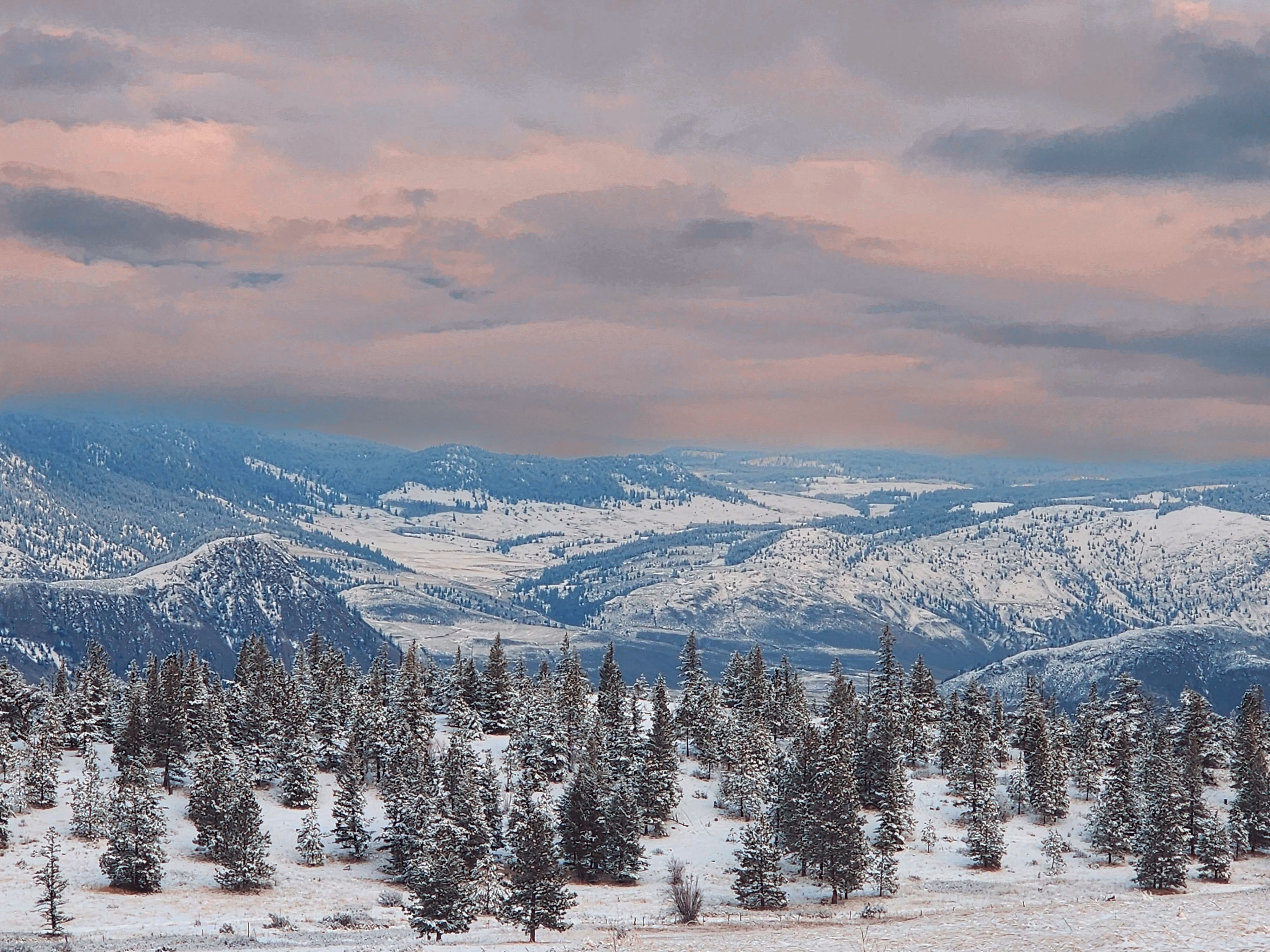 An orange sunset sets over a snowy, blue mountain range