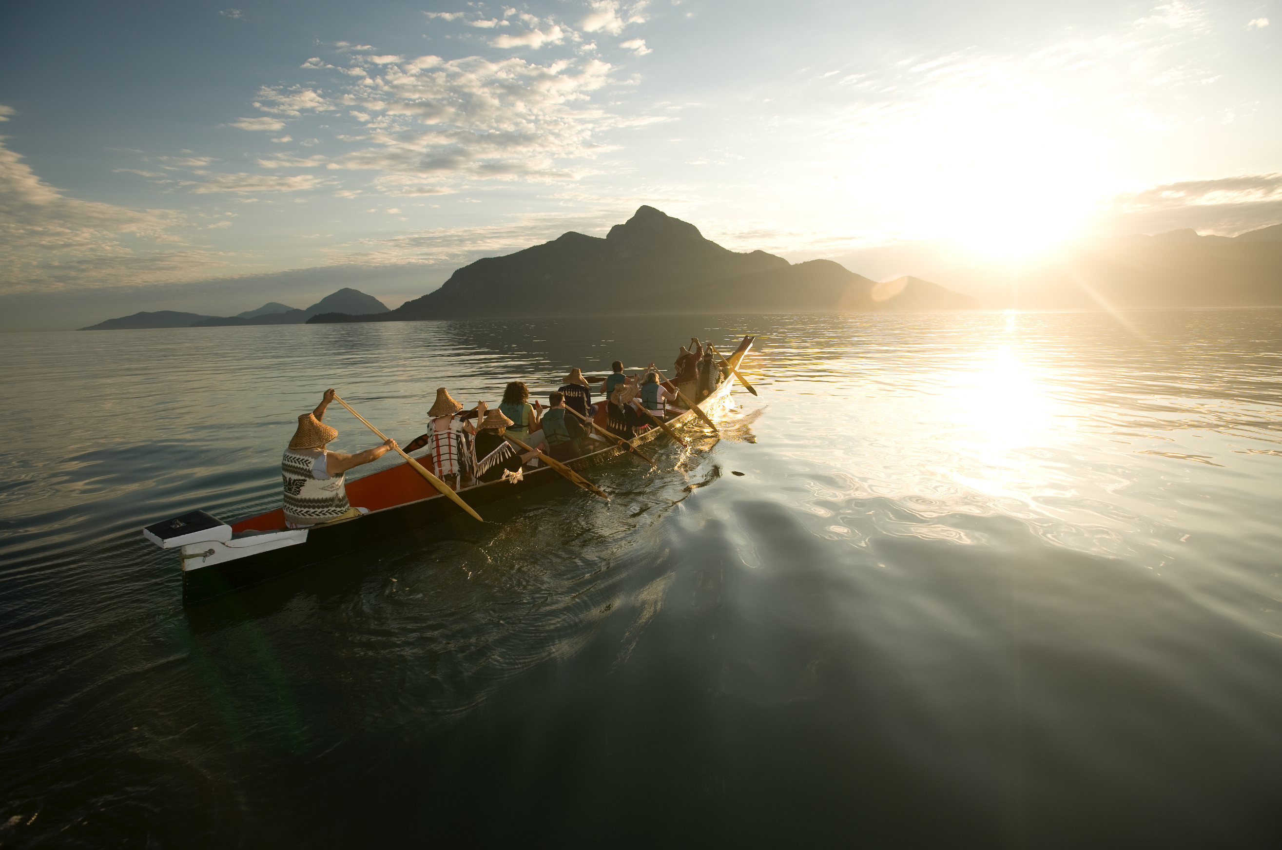 A crew of people row a boat across open water