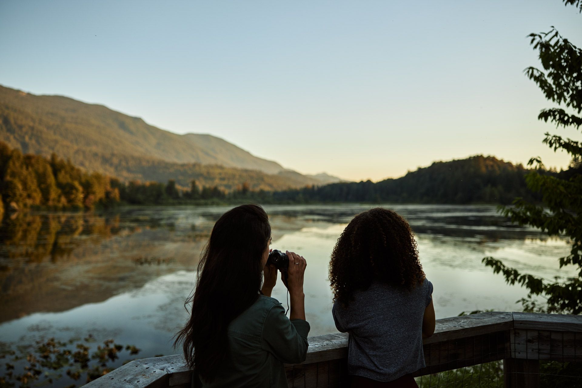 Two people use a binoculars to gaze upon a lake