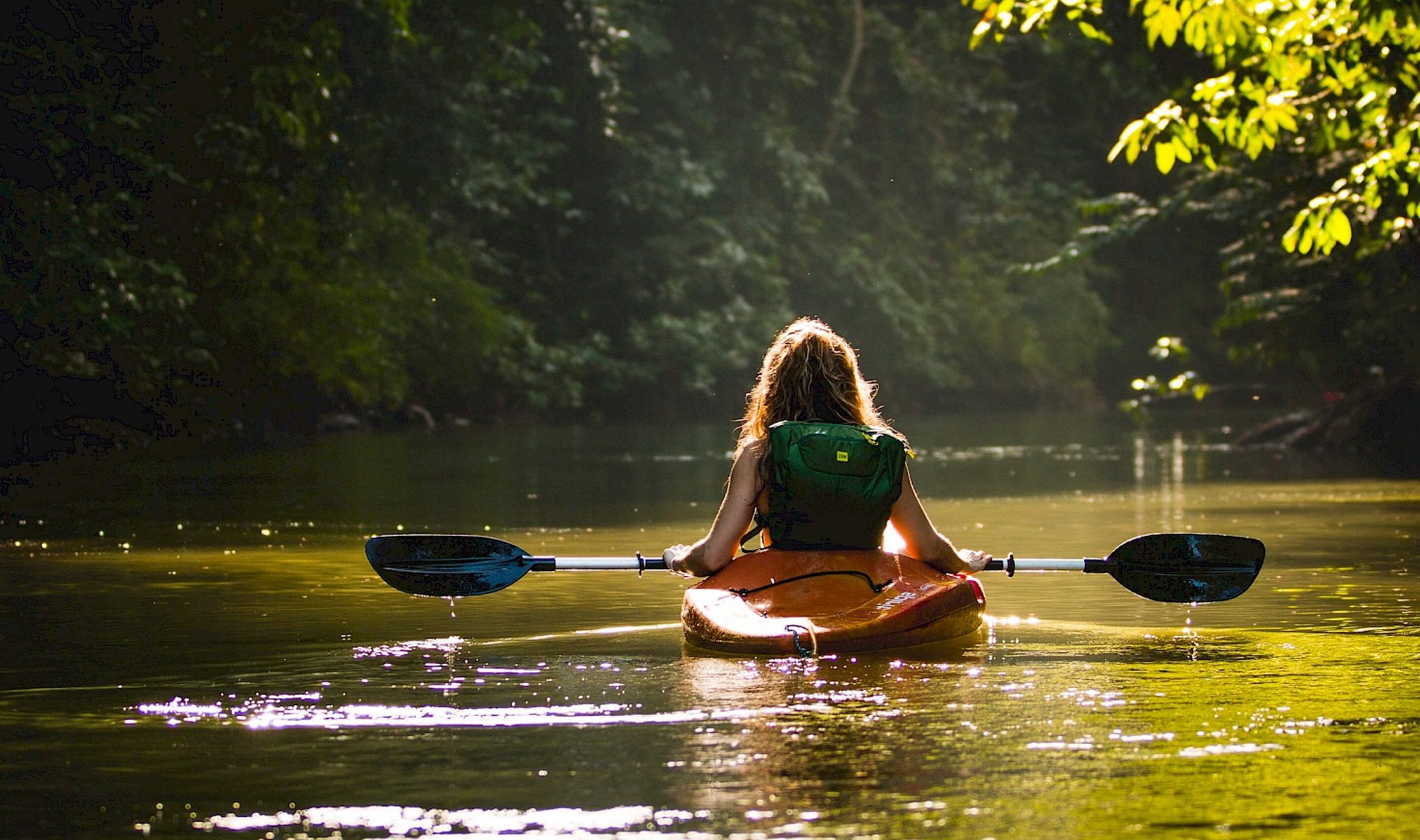 A person kayaks downstream in under sunlight