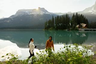 Two people walk alongside crystal blue water in a mountainous region