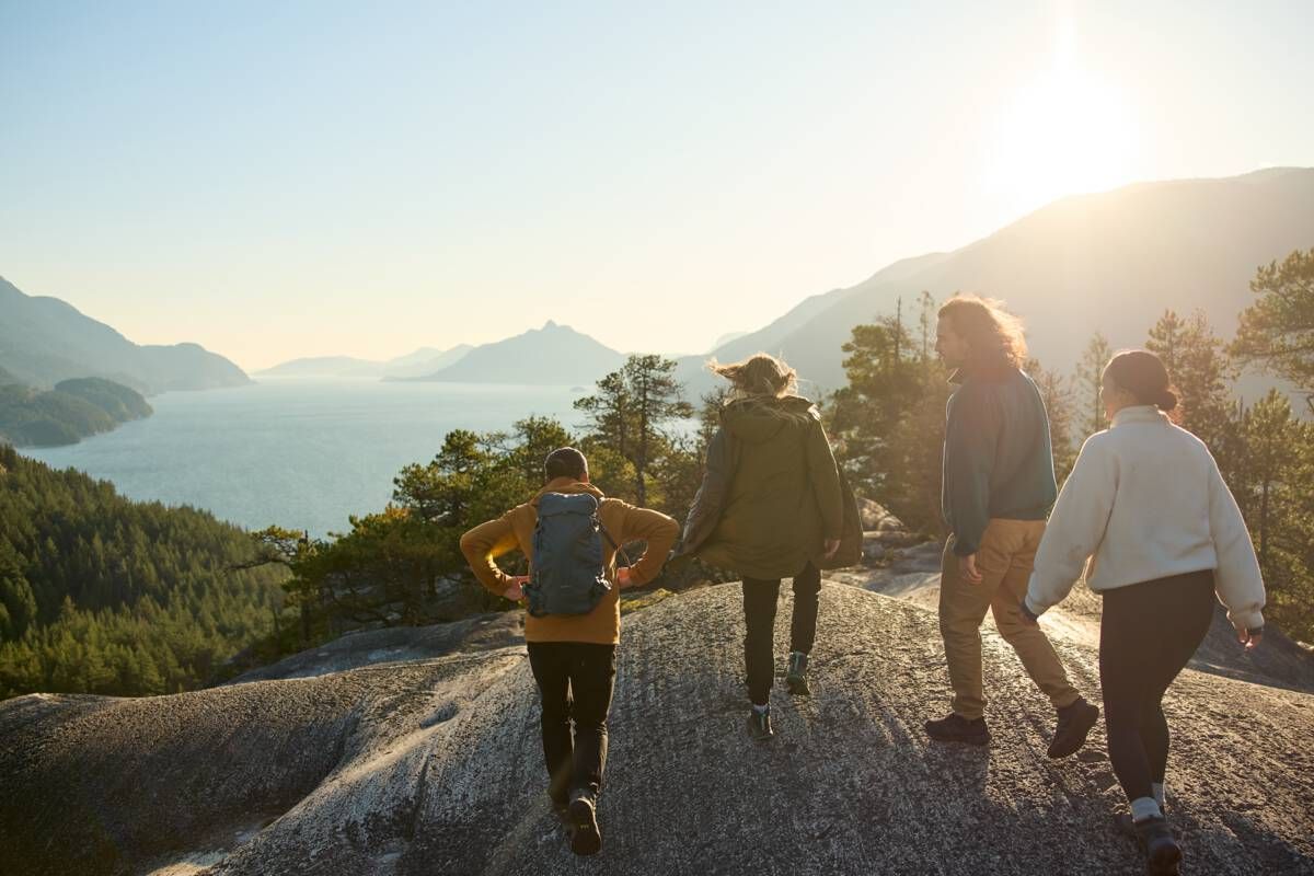 Group of hikers walking on a rocky viewpoint overlooking a coastal landscape.
