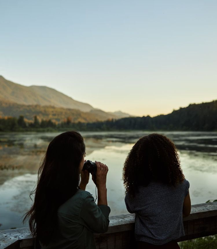Two people use a binoculars to gaze upon a lake