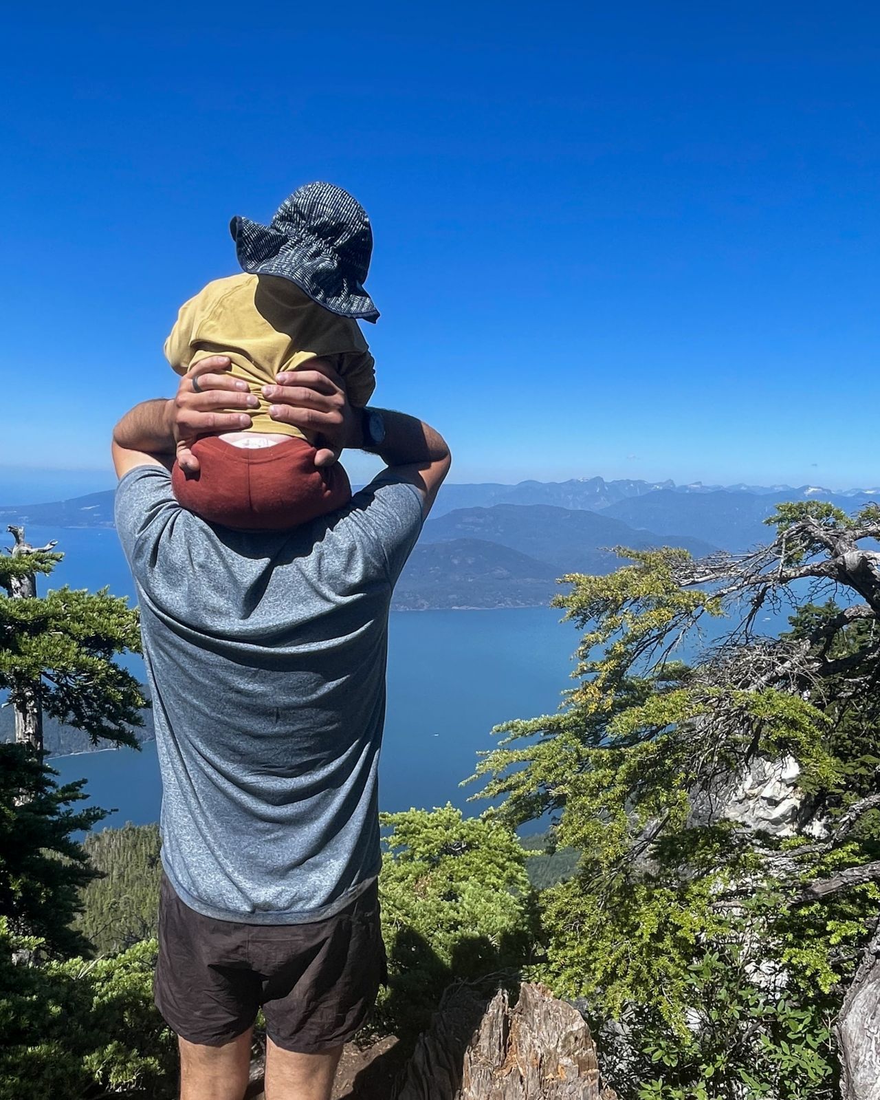 Child sits on man's shoulders and looks over Howe Sound