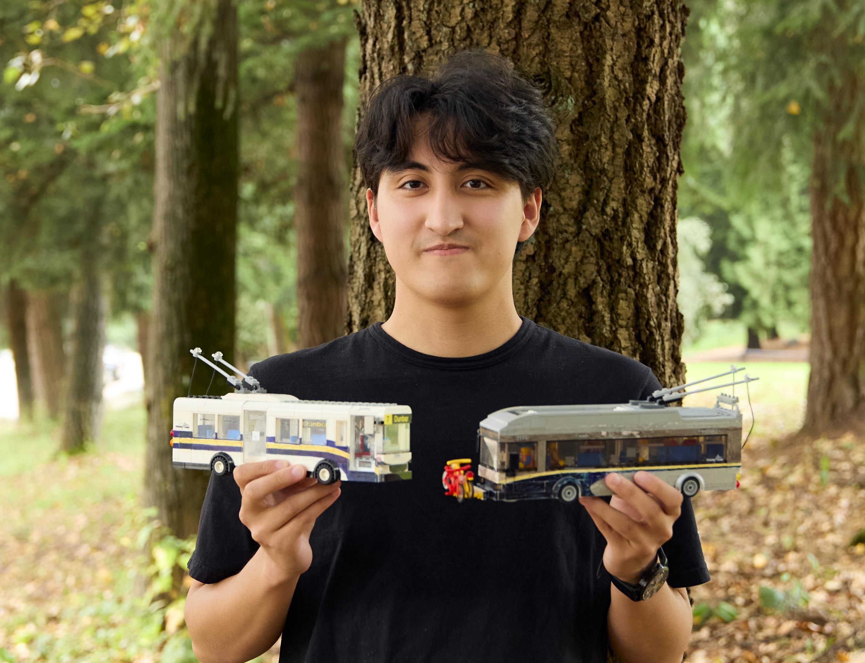 Man holds up two LEGO buses in nature
