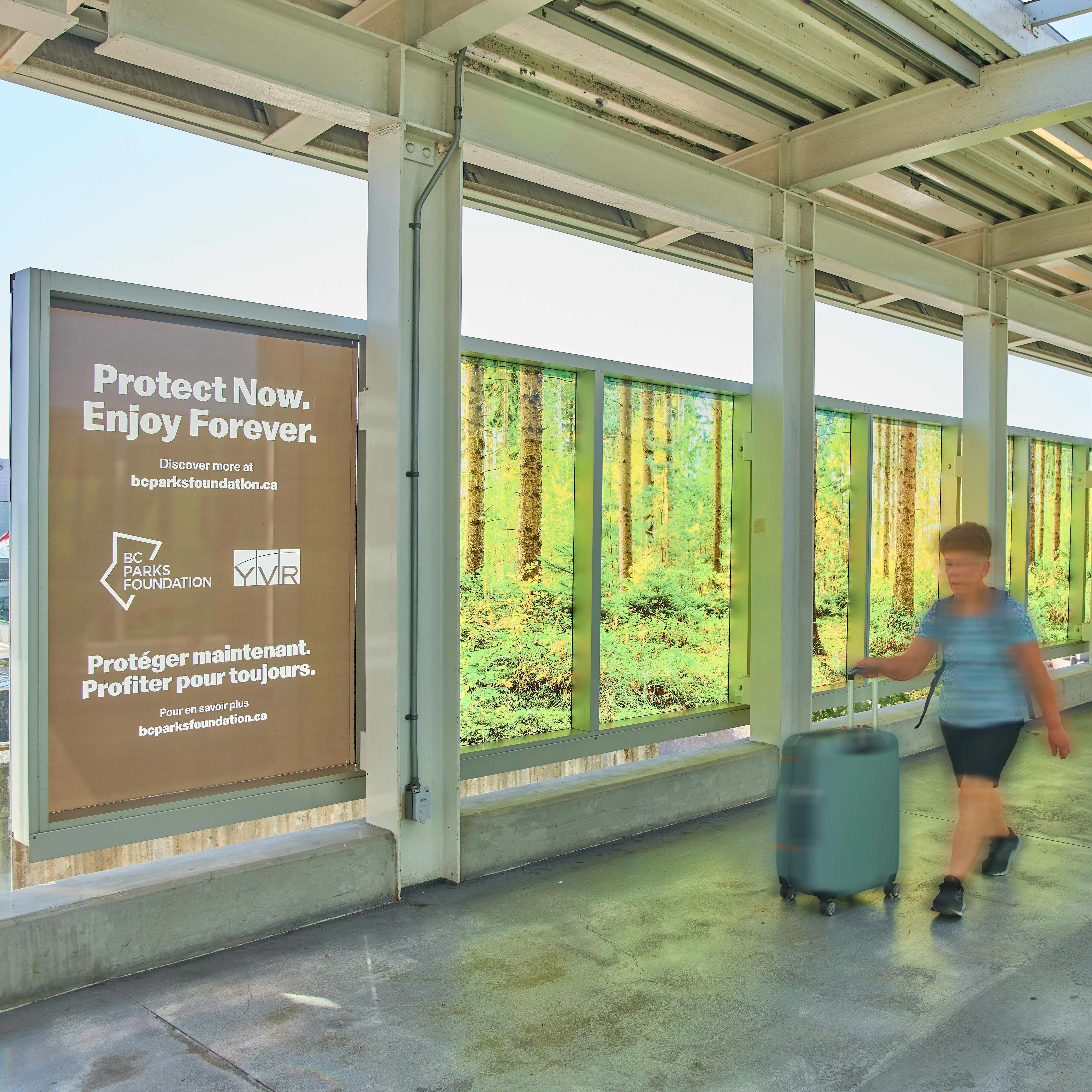 Tourist walks through Canada Line walkway with BC Parks Foundation wrap in background