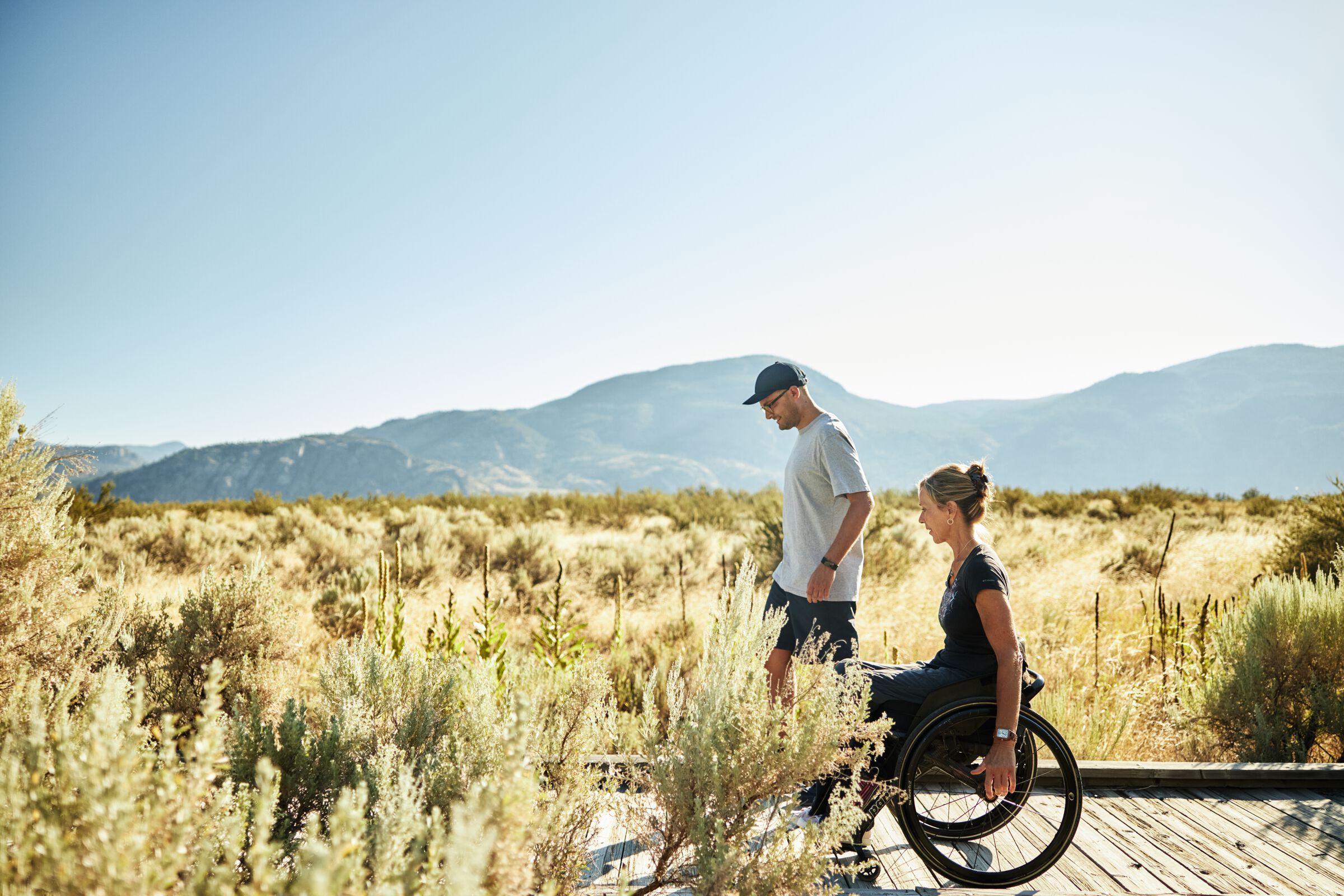 Two people on a wooden trail, one person is using a wheelchair