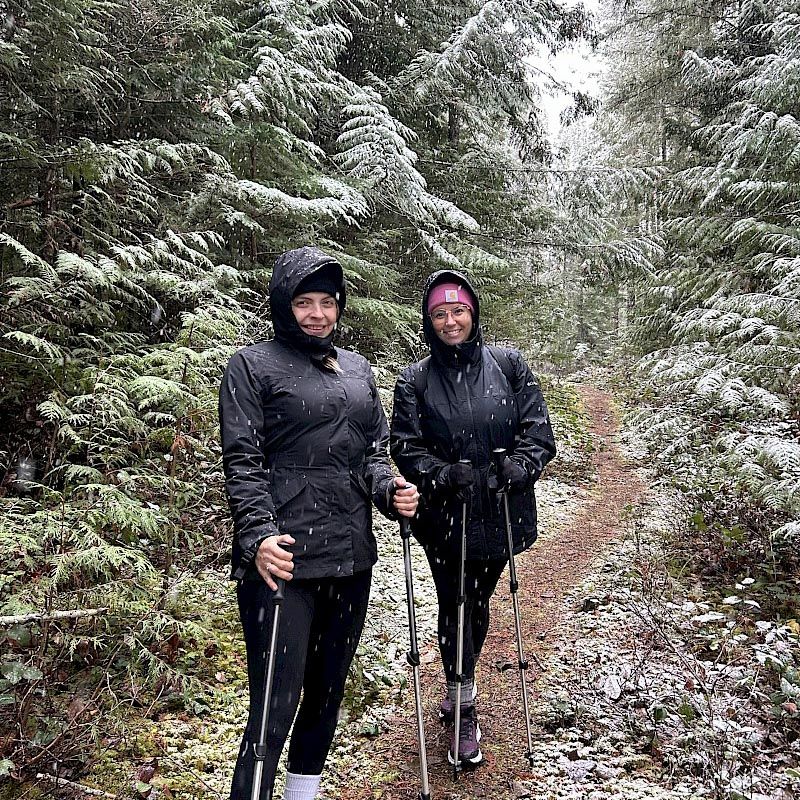 Two women stand on a snowy trail with hiking poles