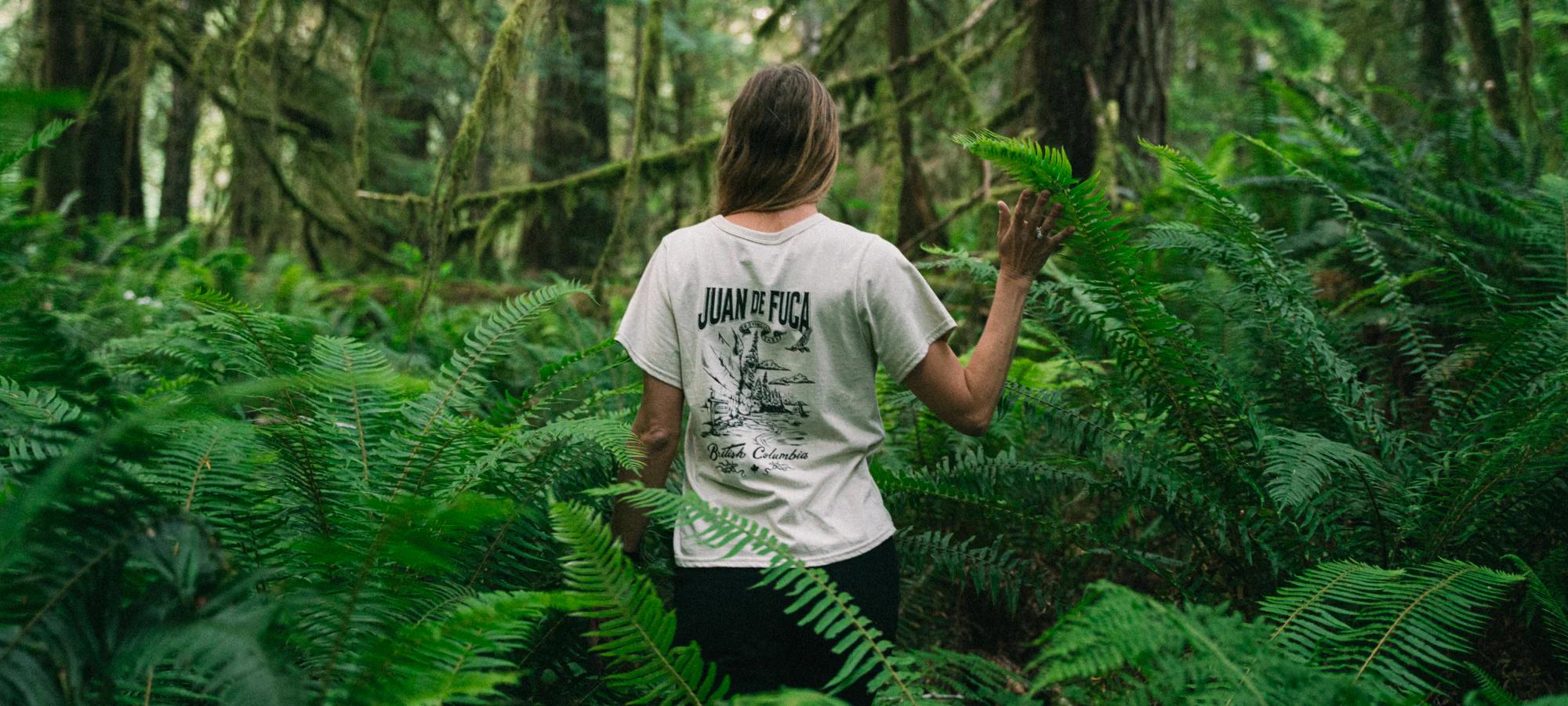 A person walks through a leafy forest wearing a BCPF shirt