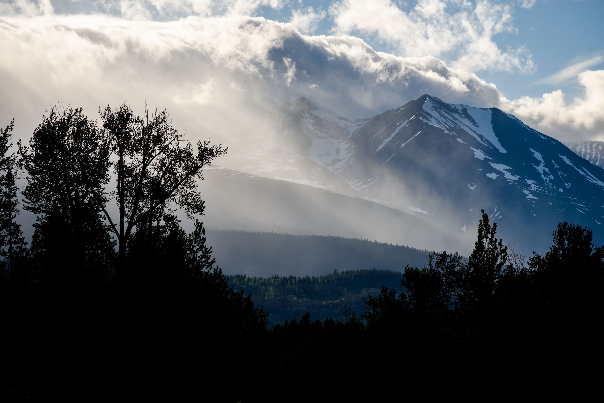 A cloudy sunset sets over snowcapped mountains.