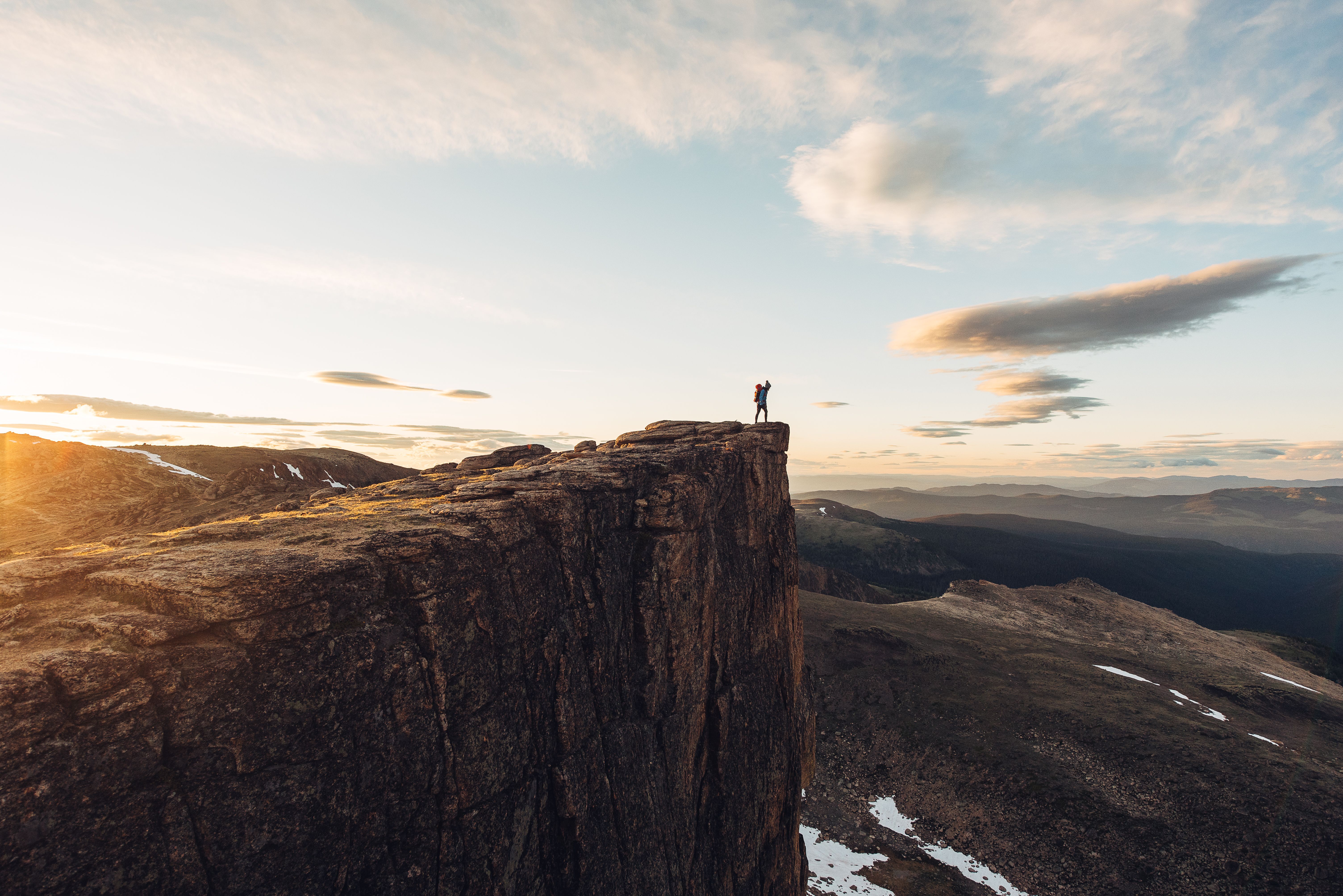 A person stands atop a large cliff, overlooking a deep valley