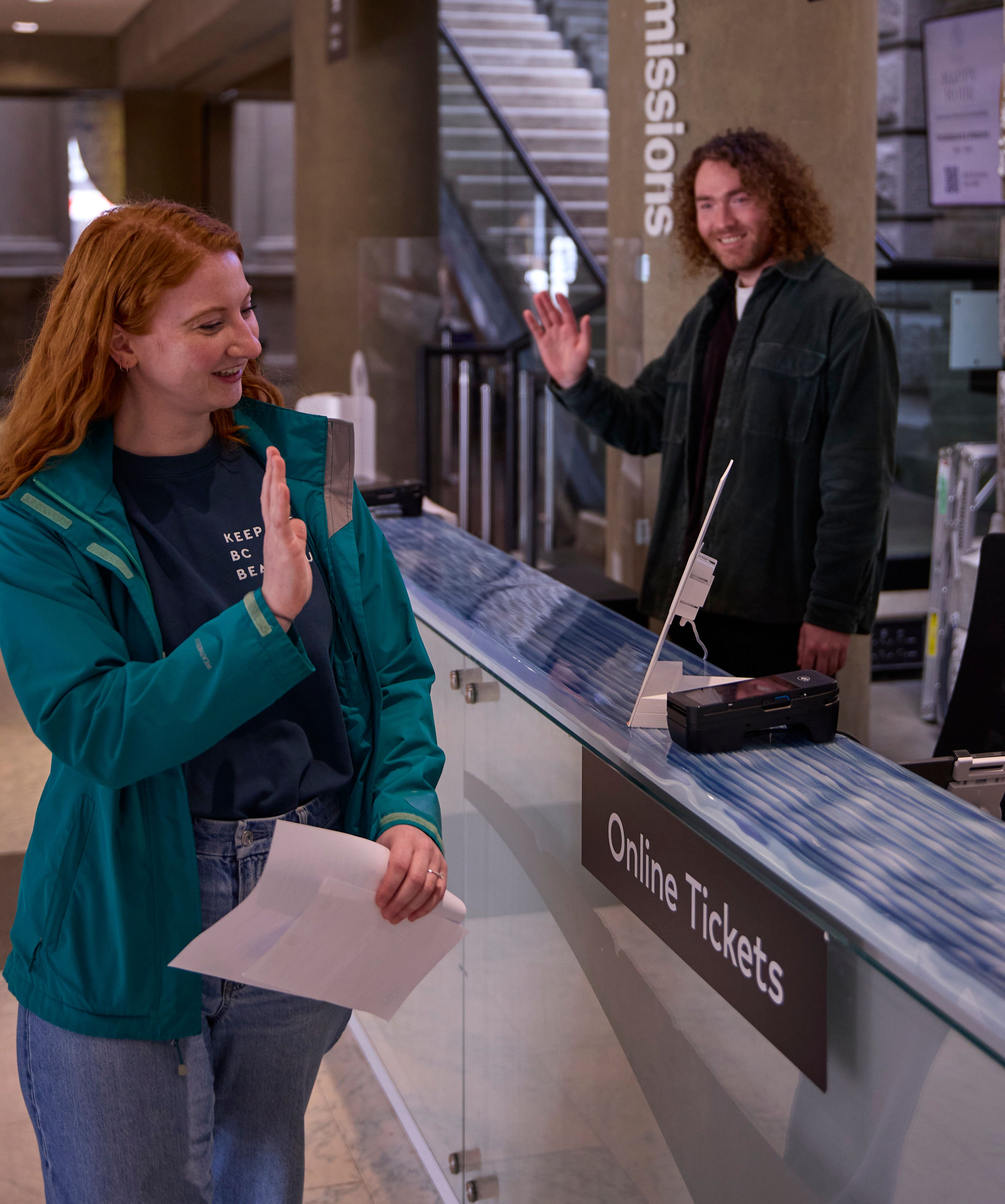 Two people waving to each other at ticket counter