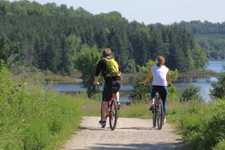 Two people bike on a bike path through nature
