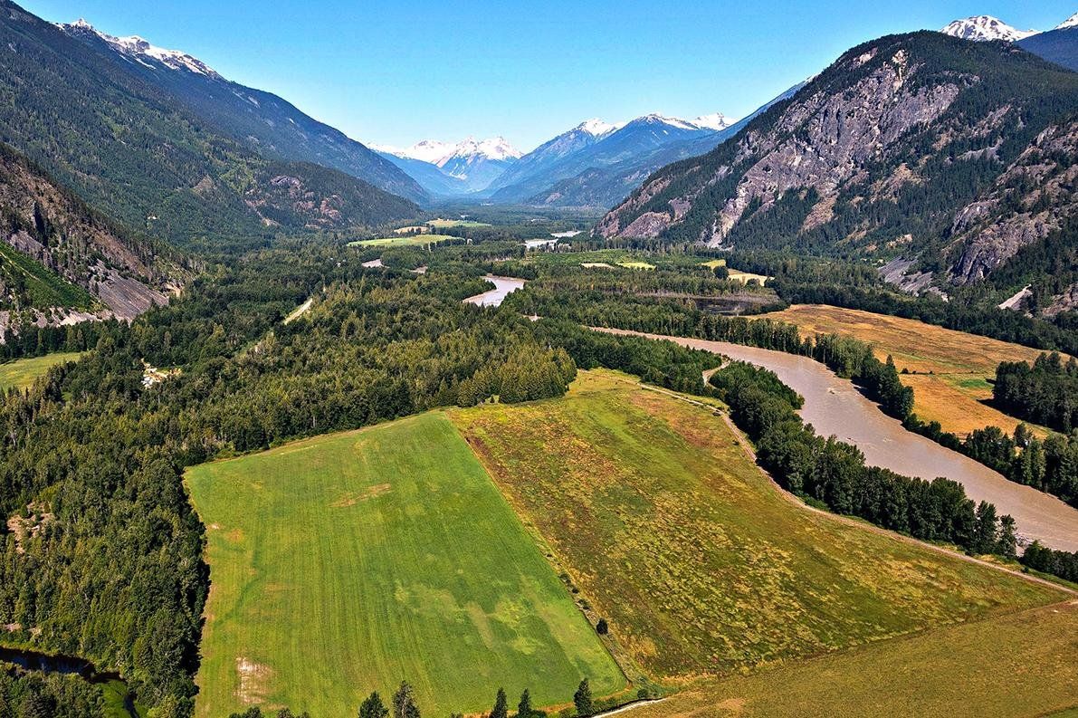 Aerial view of the Pemberton Valley with winding rivers, forested mountains, and farmland under a clear blue sky.